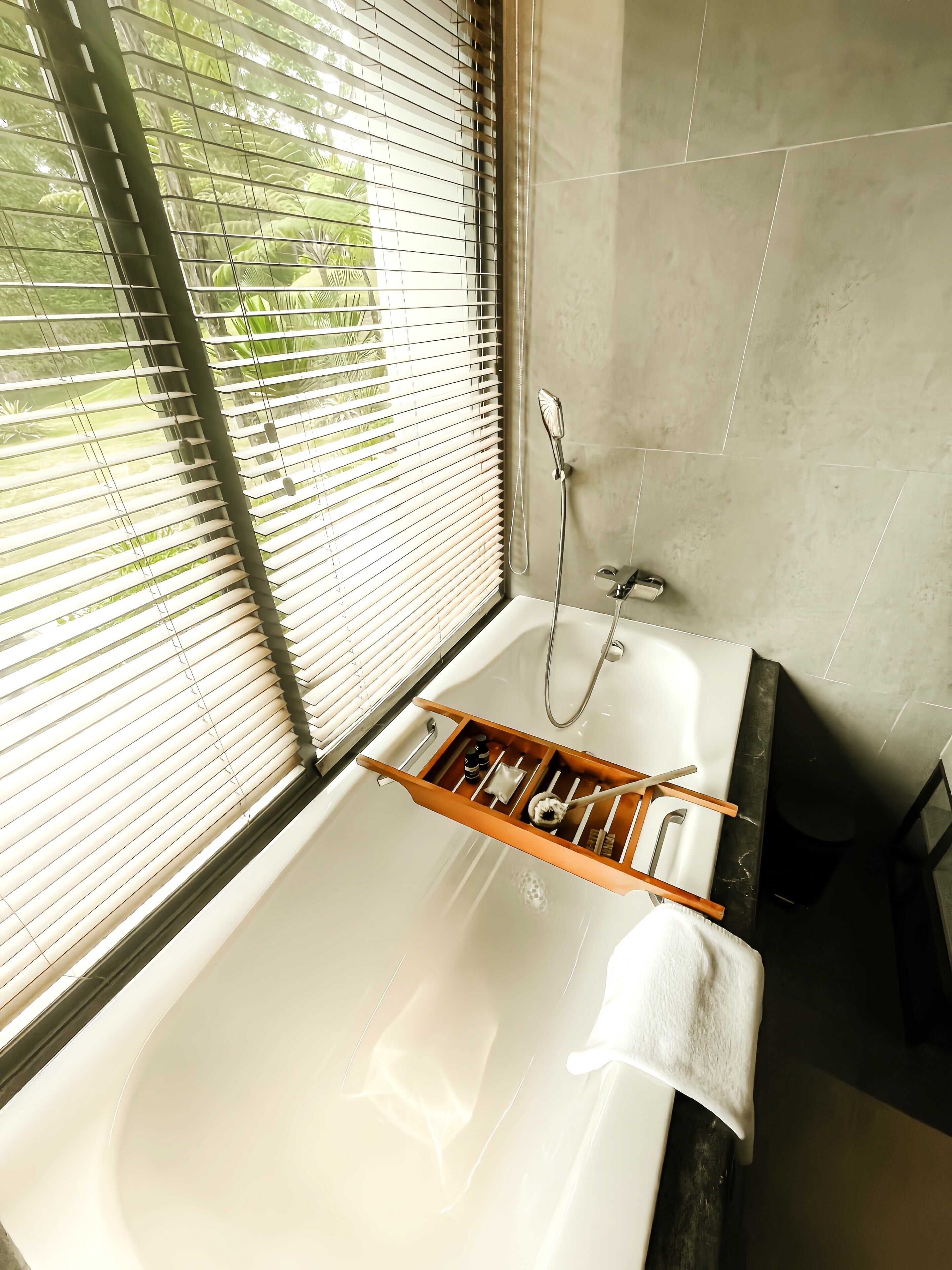 A bathroom with a bathtub, a window with blinds, and a towel rack.