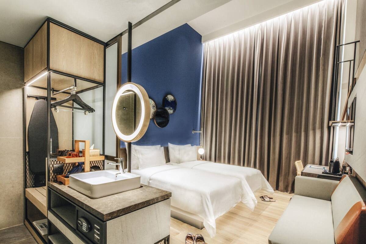 A hotel room with a large bed, a bedside table with a mirror, a sofa, and a desk with a lamp.
