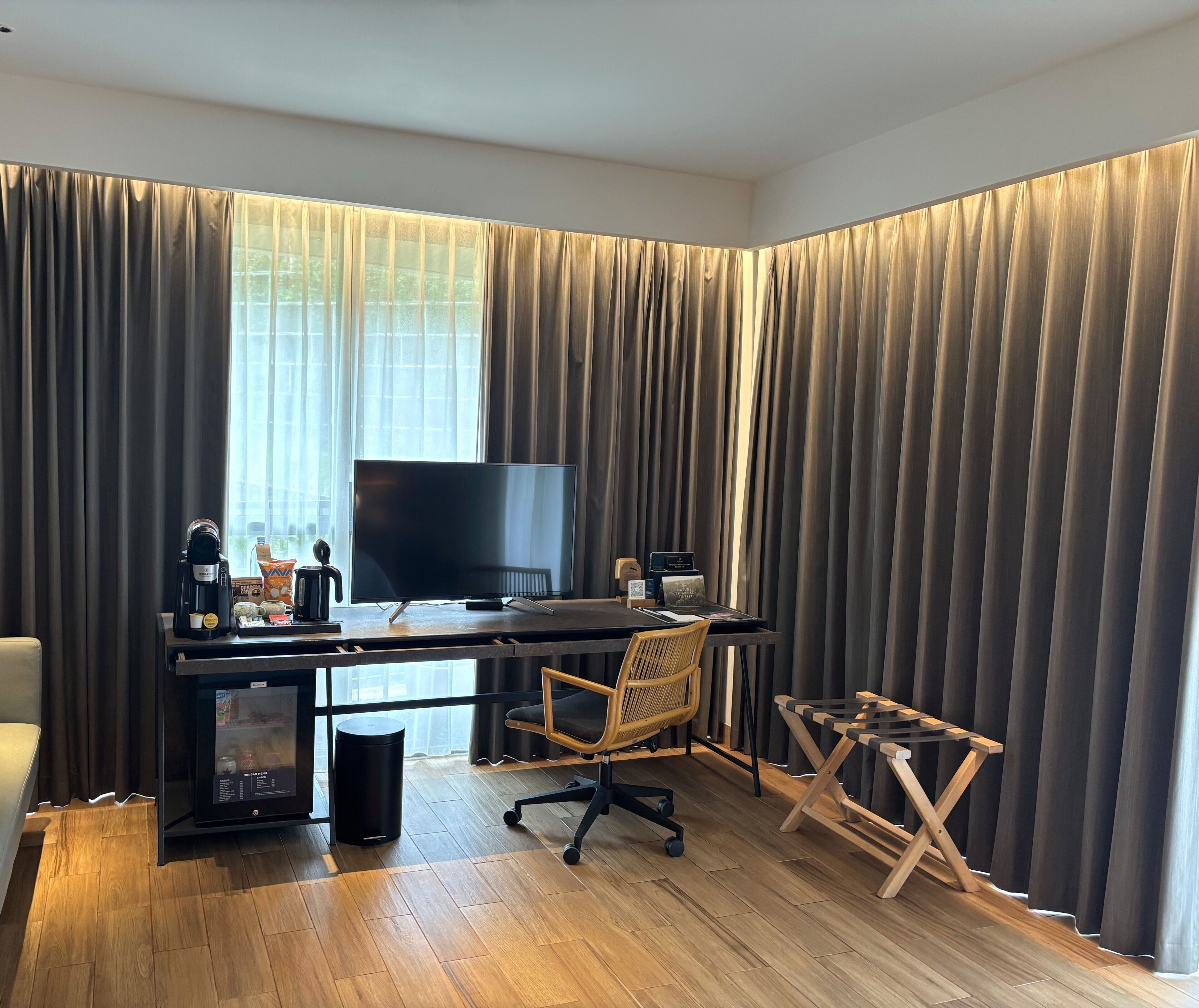 A modern hotel room with a wooden desk, a flat-screen TV, a coffee maker, and a chair.