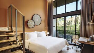Una habitación de hotel moderna con una cama grande, una escalera de madera, un escritorio con una silla y ventanas amplias que ofrecen vistas al exterior.