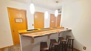 A kitchen with a wooden island, bar stools, pendant lights, and wooden doors.