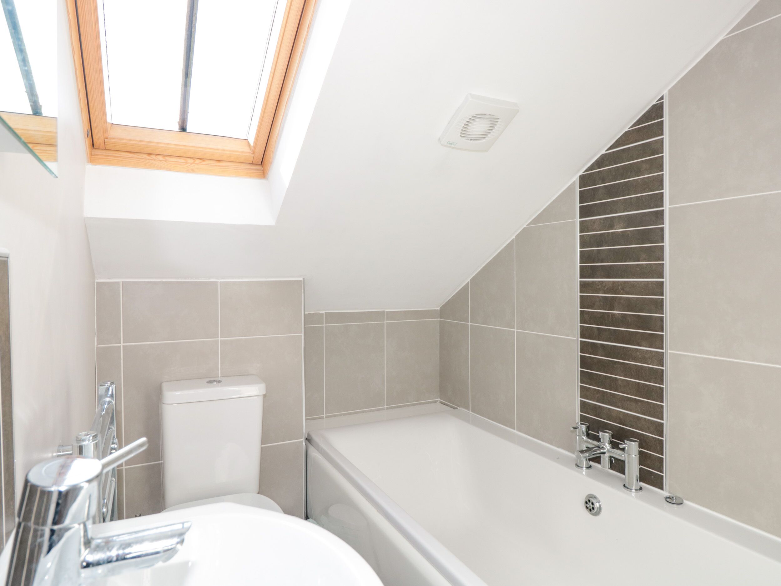 A modern bathroom with a skylight, a bathtub, and a toilet.