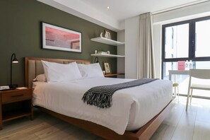 Et moderne hotelværelse med en stor seng, sengeborde, et natbord, et billede i ramme på væggen, et vindue med udsigt og en stol ved vinduet.