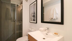 A modern bathroom with a glass shower enclosure, a white toilet, a sink with a mirror above it, and a framed picture on the wall. - w*| Spacious Loft w/AC in Barranco (Barranco)