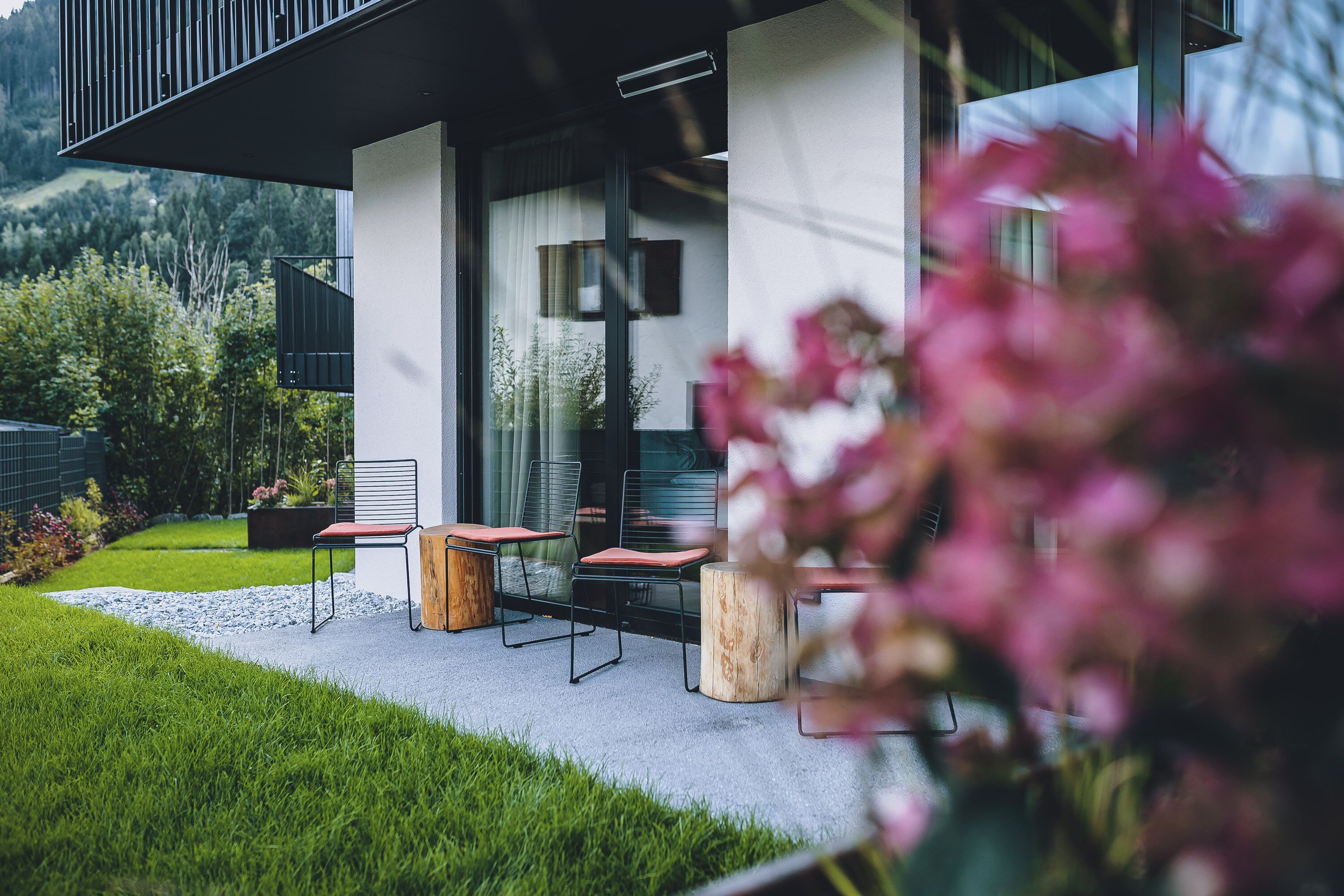 A modern outdoor seating area with a glass door entrance, a concrete patio, and a view of a mountainous landscape.