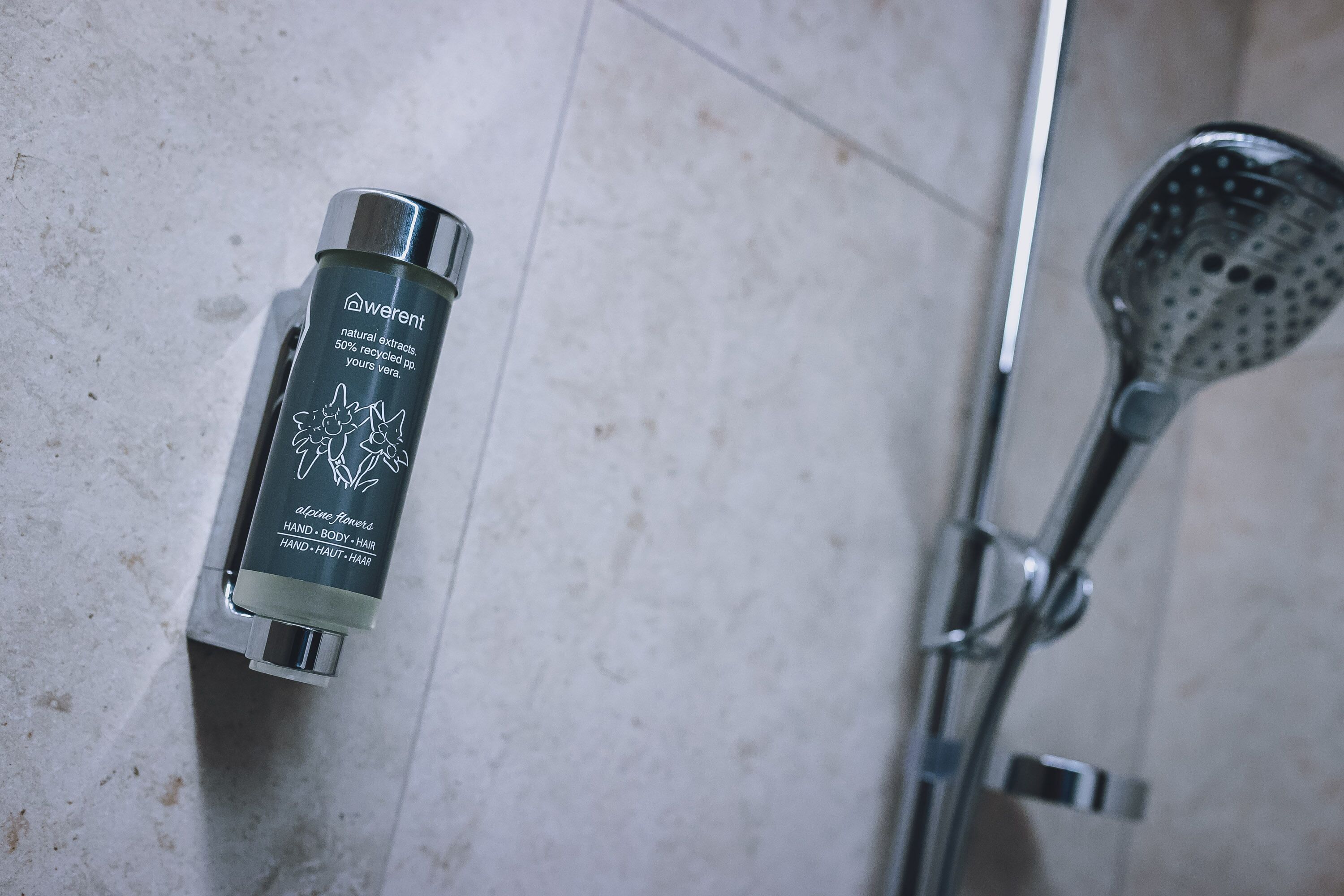 A bathroom with a shower, a wall-mounted bottle of hand, body, and hair care product.