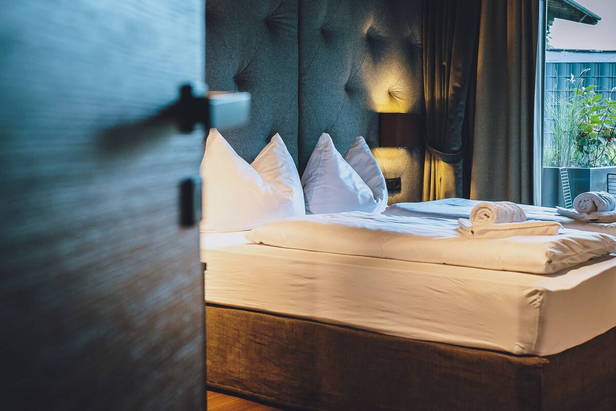 Een net opgemaakt bed met witte lakens en kussens, een gestoffeerd hoofdbord en een bedlampje.