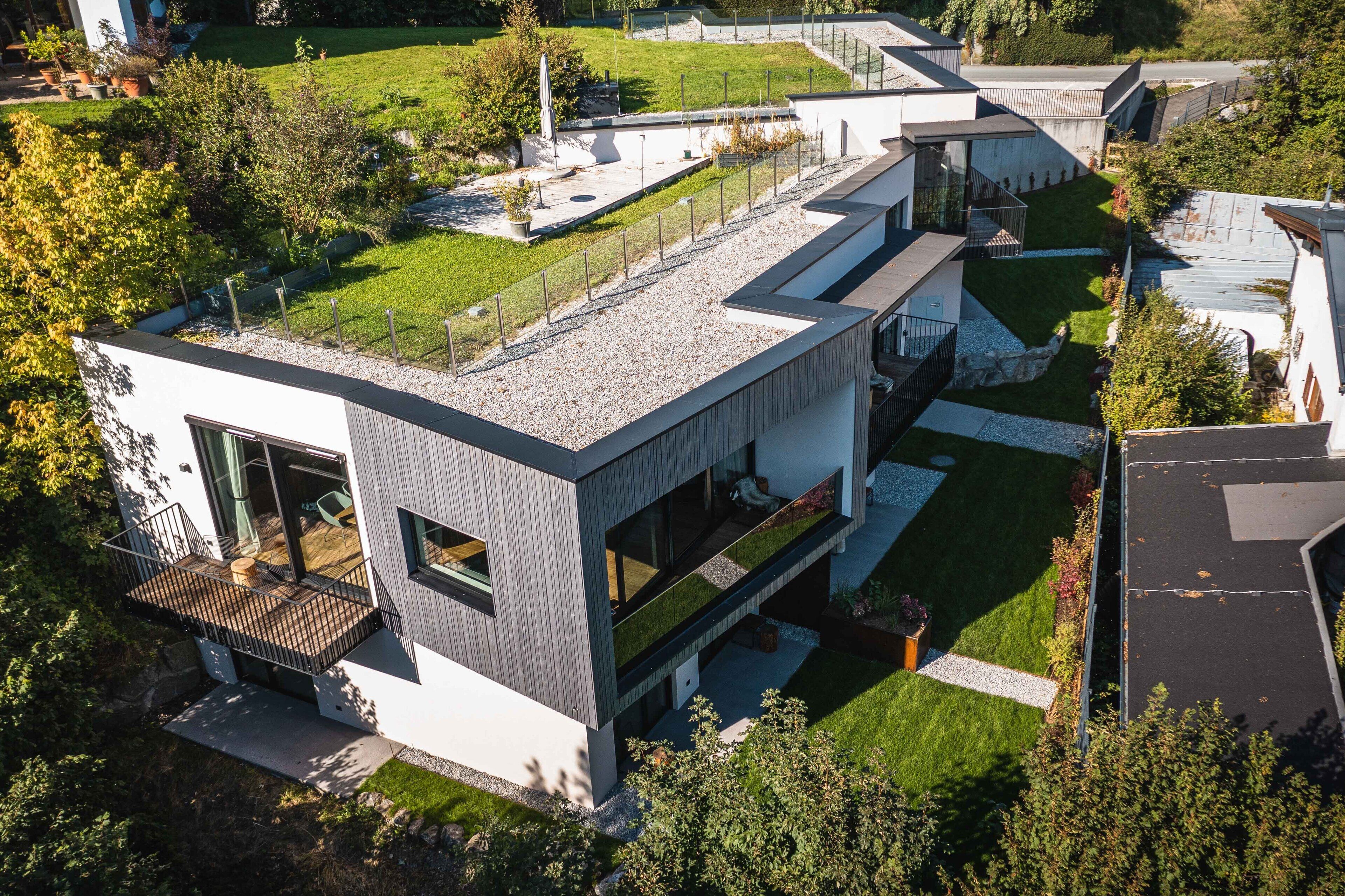 A modern two-story house with a flat roof, large windows, and a balcony.