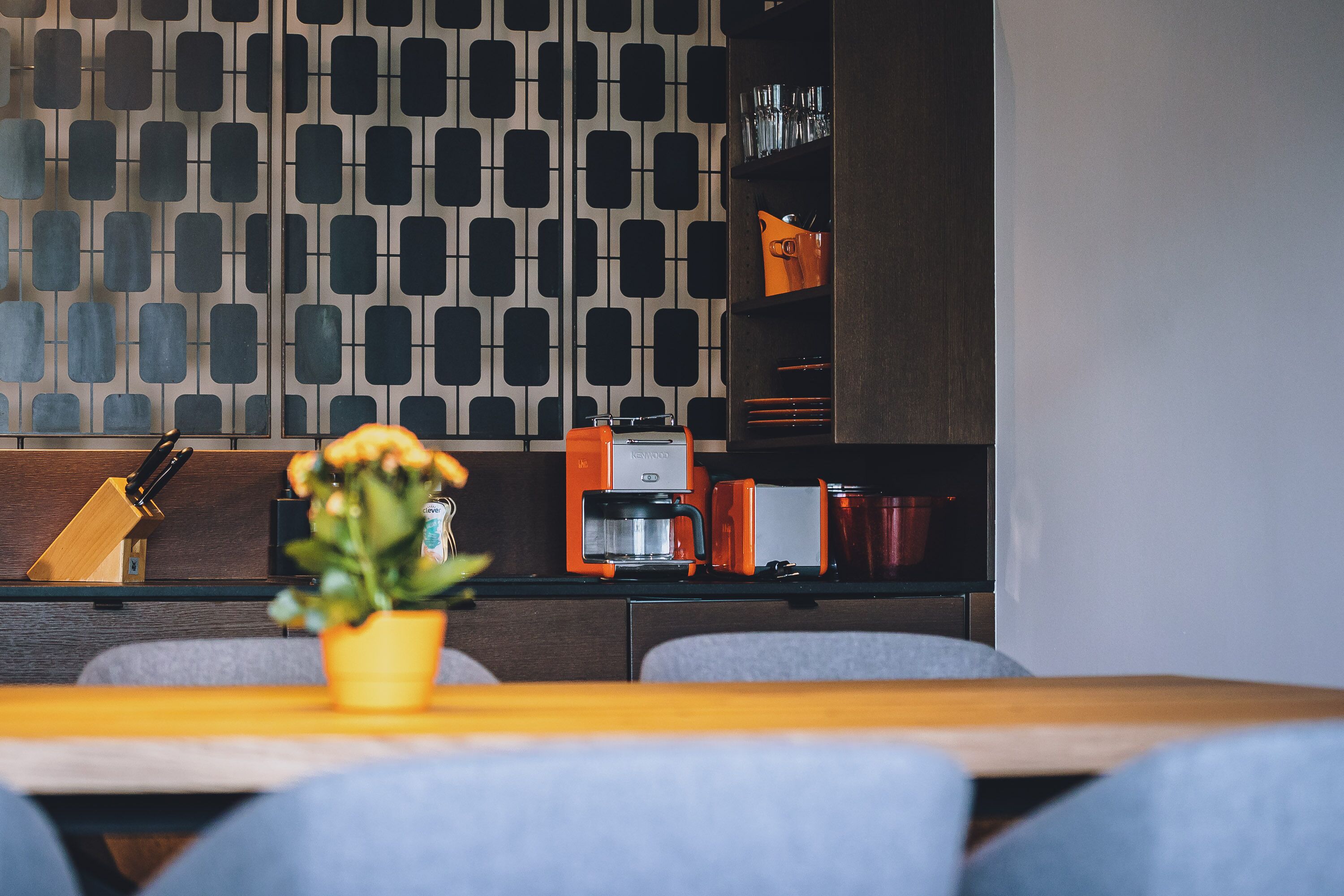 Et moderne køkken med et mønstret backsplash, en kaffemaskine og en potteplante på bordet.