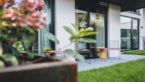 Un espace extérieur moderne aménagé avec des chaises et une table, entouré d’une pelouse bien entretenue et de plantes en pot.