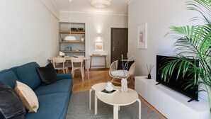 A modern living room with a sofa, coffee table, TV, and a dining area with chairs and a table. - Absolute 2BR Apartment (Athens)