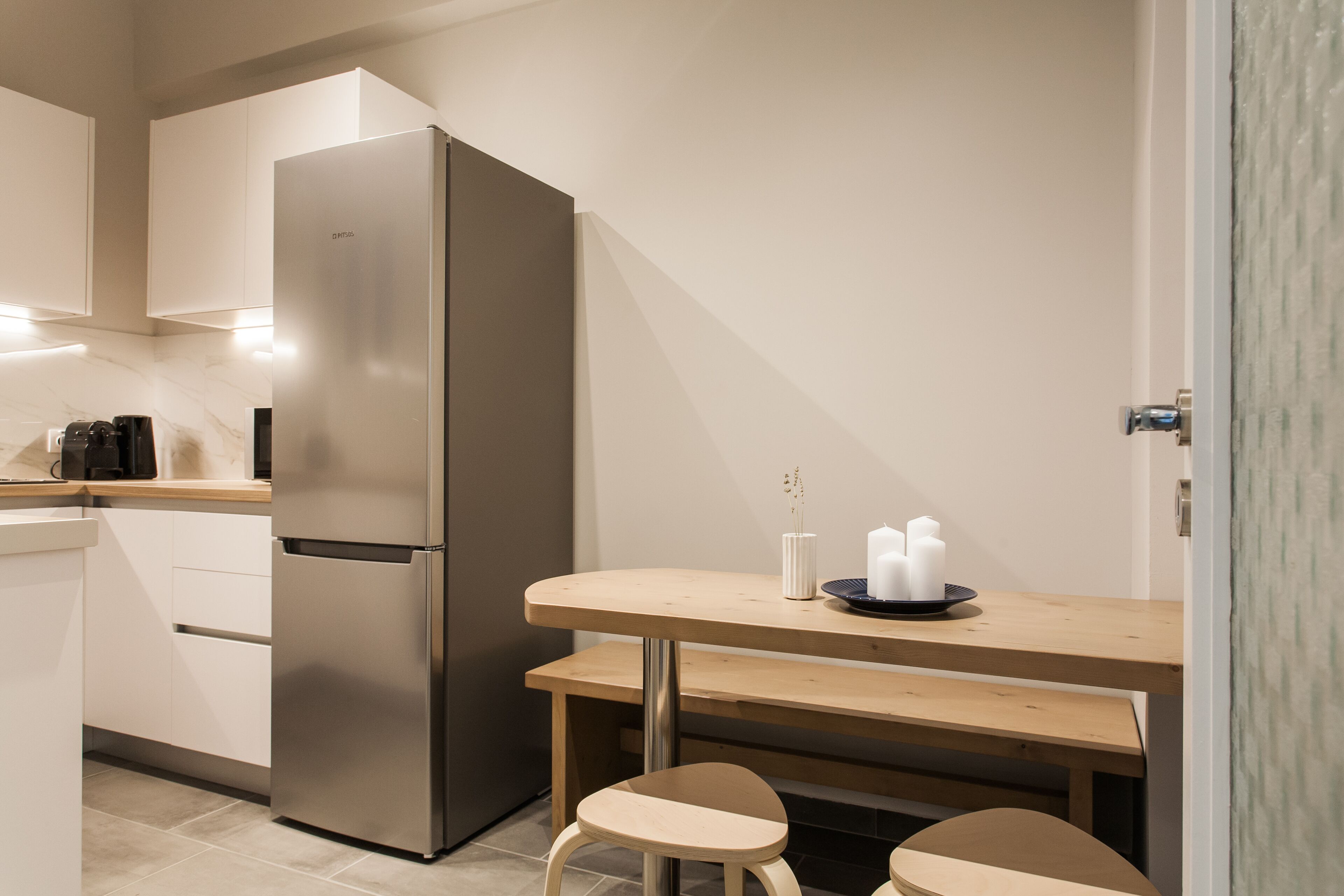Une cuisine compacte dotée d’un réfrigérateur en acier inoxydable, d’un plan de travail en bois et d’un petit coin repas avec deux tabourets.