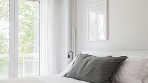 A bedroom with a bed, a window with curtains, a wall-mounted light, and a framed picture. - Absolute 2BR Apartment (Athens)