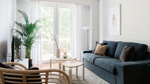 A modern living room with a sofa, two side tables, a potted plant, and a large window with curtains. - Absolute 2BR Apartment (Athens)