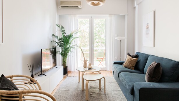A modern living room with a sofa, a small table, a TV, and a potted plant. - Absolute 2BR Apartment (Athens)