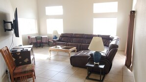 Een woonkamer met een bank, fauteuil, salontafel en een aan de muur bevestigde televisie.