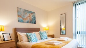 A hotel room with a bed, a nightstand, a framed certificate, a painting, a mirror, and a window with blinds. - ByEvo 5 Brabloch GLA Apartment  (Paisley)