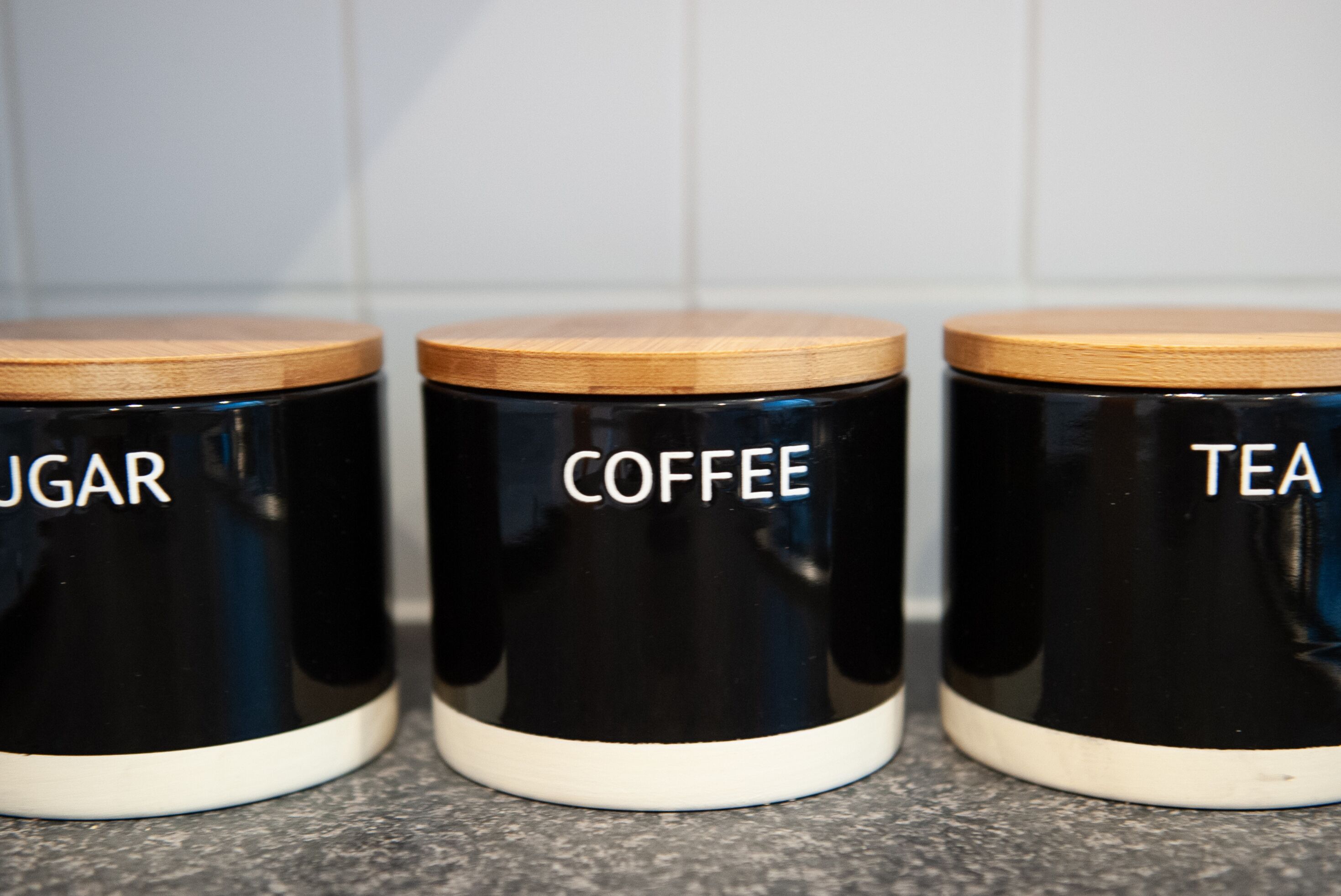 Trois récipients noirs à couvercles en bois, étiquetés respectivement « SUCRE », « CAFÉ » et « THÉ ».