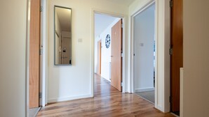 A hallway with wooden flooring, white walls, and doors leading to other rooms. - ByEvo 5 Brabloch GLA Apartment  (Paisley)