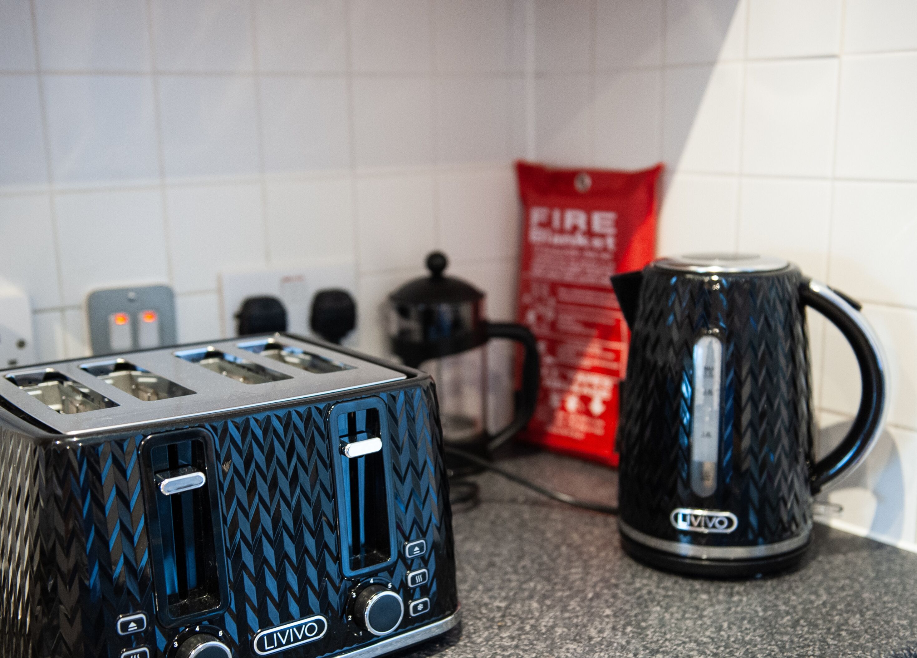 A kitchen with a black toaster, a black coffee maker, and a red fire extinguisher.