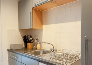 Una cocina con armarios blancos, un lavamanos de acero inoxidable y un escurreplatos.