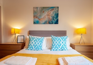 Habitación de hotel con cama, dos mesitas de noche, un certificado enmarcado y un cuadro en la pared.