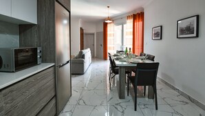 A modern kitchen with a built-in microwave and refrigerator, a dining area with a table set for four, and a living room with a sofa and a TV. - A Bed of Roses (Żebbuġ)
