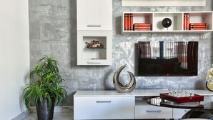 A modern living room with a white entertainment unit, a large flat-screen TV, a potted plant, and a decorative metal sculpture. - A Bed of Roses (Żebbuġ)