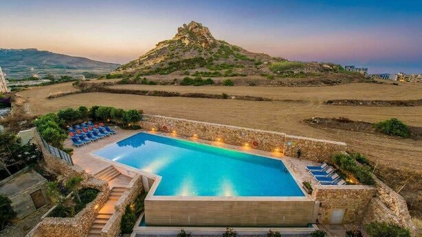 A rectangular pool with a stone border, surrounded by lounge chairs and a stone wall. - A Bed of Roses (Żebbuġ)