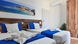 A hotel room with two beds, a wooden headboard, a painting of a beach, an air conditioning unit, and a wooden wardrobe. - A Bed of Roses (Żebbuġ)