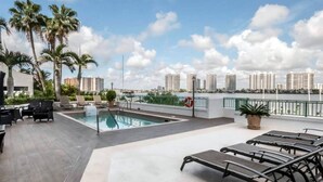 A rooftop pool area with lounge chairs, a pool, palm trees, and a city skyline view. - Le Montcalm 102 STR-01921 (Sunny Isles Beach)