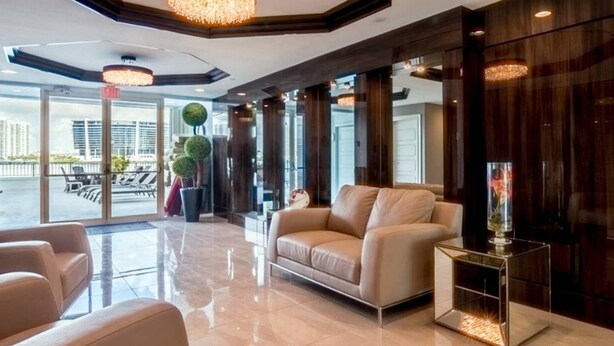 A modern lobby with a leather sofa, a glass coffee table, and a chandelier. - Le Montcalm 102 STR-01921 (Sunny Isles Beach)