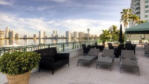 A rooftop terrace with lounge chairs, a potted plant, and a view of a city skyline across a body of water. - Le Montcalm 102 STR-01921 (Sunny Isles Beach)