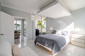 A hotel room with a bed, a sofa, a balcony with a view of palm trees and buildings, and a door leading to another room. - Le Montcalm 102 STR-03618 (Sunny Isles Beach)