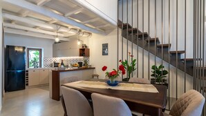 A modern kitchen with a dining area, featuring a wooden table, chairs, and a staircase with metal railings.
