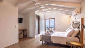 A bedroom with a bed, wooden floor, white walls, and a balcony with a view.