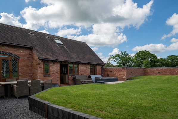 A brick building with a sloped roof, outdoor seating area, and a hot tub.