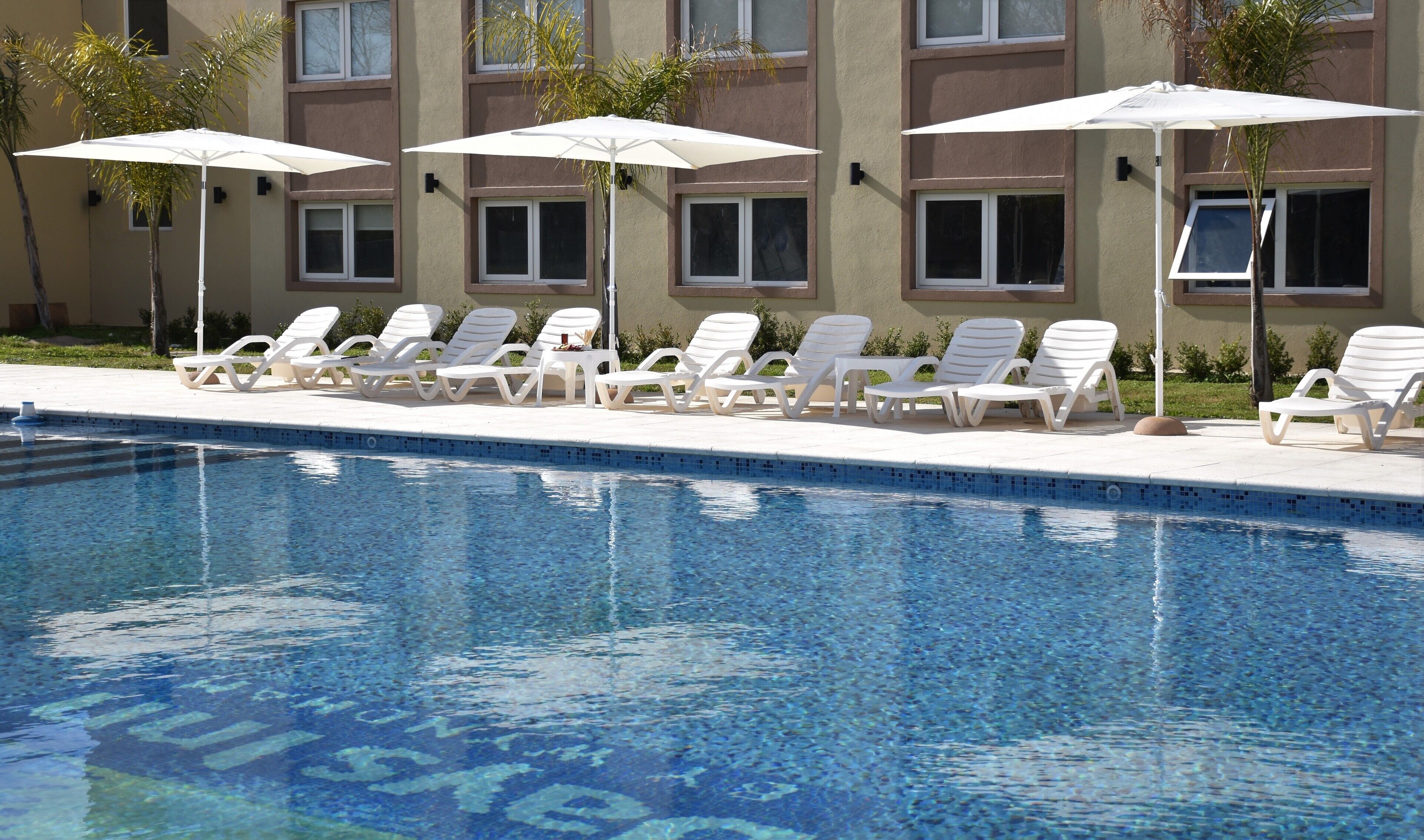 A poolside area with lounge chairs and umbrellas, a clear pool, and a building with multiple windows.