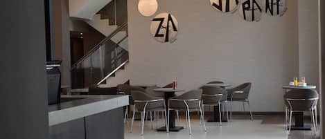 Un interior moderno con una recepción, una escalera y un comedor con mesas y sillas.