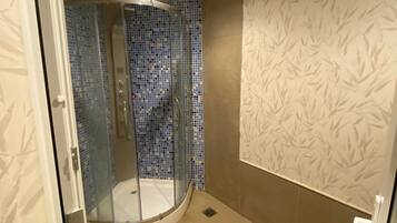 A bathroom with a glass-enclosed shower, tiled walls, and patterned wallpaper.