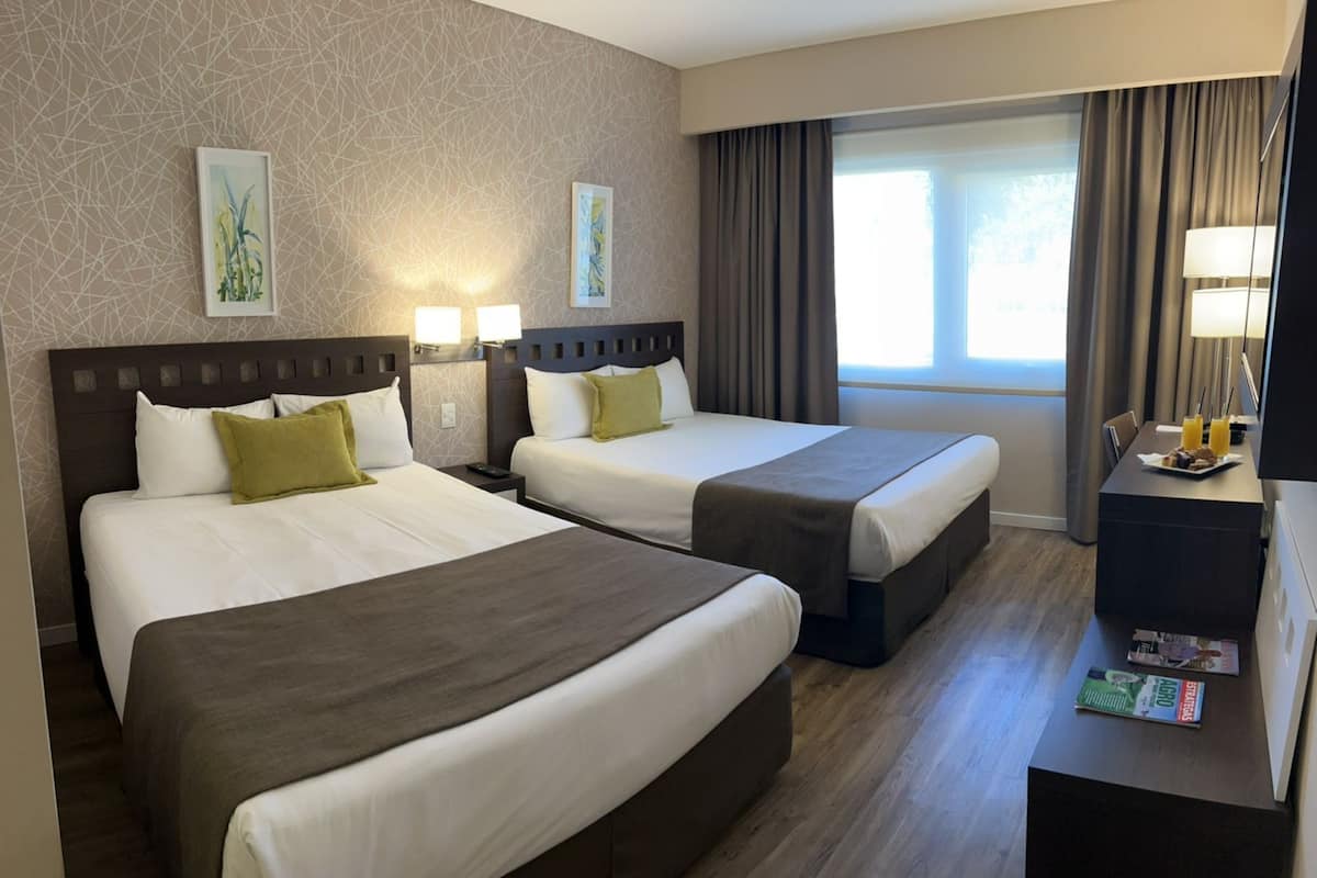A hotel room with two beds, a desk with a lamp, and a window with curtains.