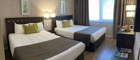 A hotel room with two beds, a desk with a lamp, and a window with curtains.