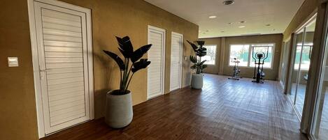 A spacious hallway with wooden flooring, large potted plants, and exercise equipment.