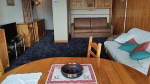 A cozy living room with a brown leather sofa, a white couch with colorful cushions, a wooden dining table with a bowl, and a TV on a stand. - APARTMENT LA TOUSSUIRE, 3 ROOMS 6/8 PEOPLE (La Toussuire)
