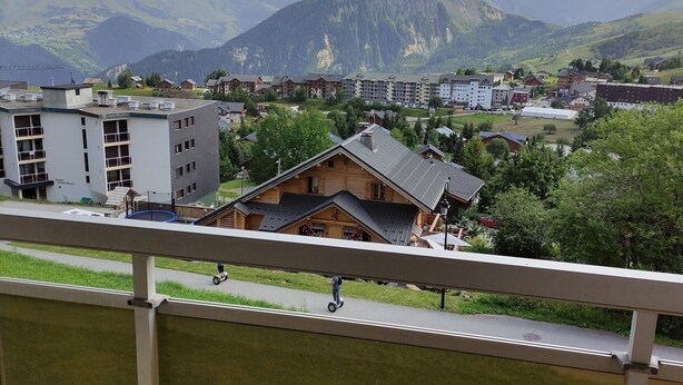 A view of a mountain town with buildings, a pedestrian path, and a mountain range in the background. - APARTMENT LA TOUSSUIRE, 3 ROOMS 6/8 PEOPLE (La Toussuire)