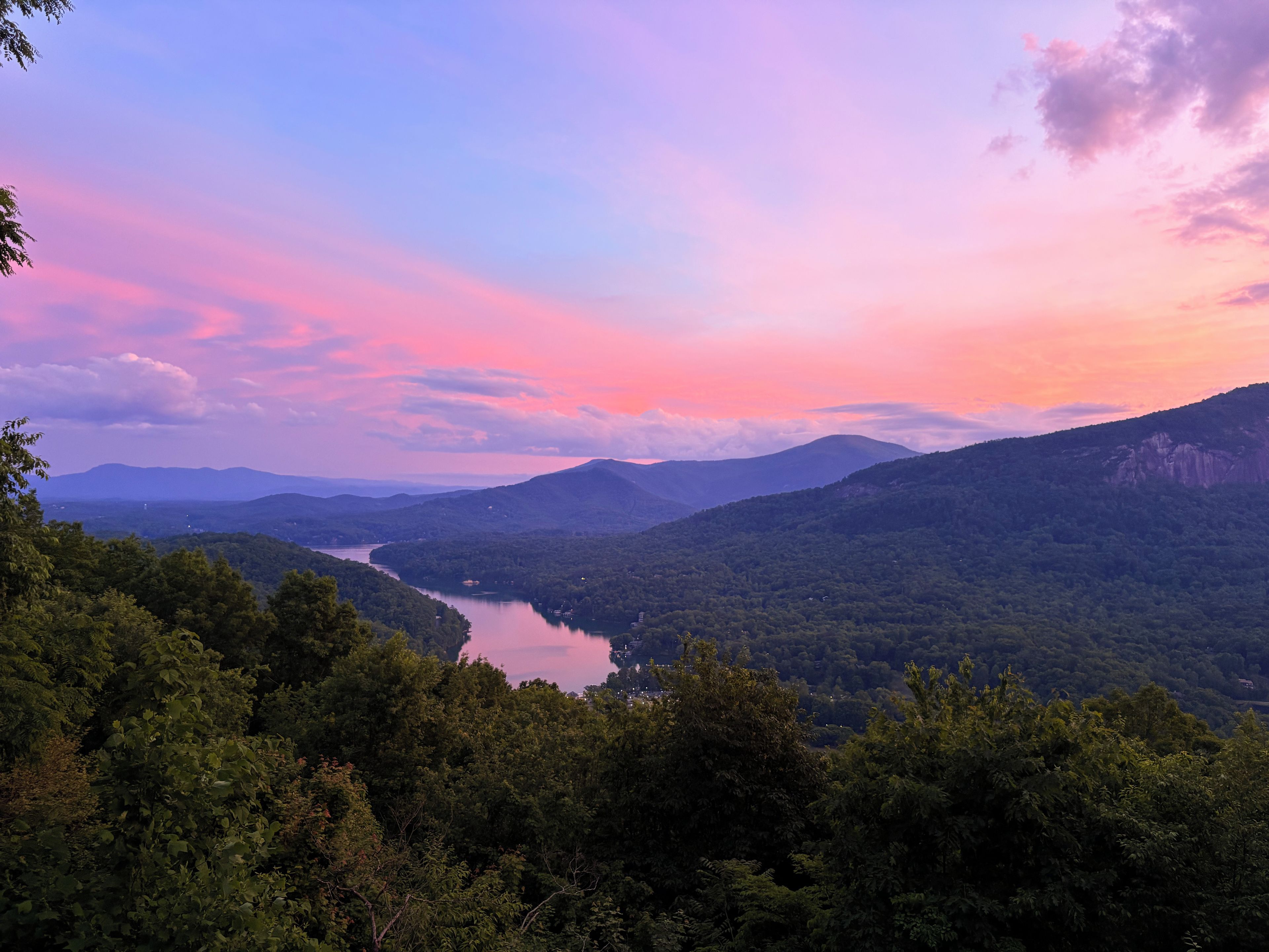 A mountainous landscape with a river, dense forest, and a clear sky.