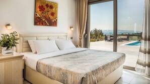 A bedroom with a large bed, a painting on the wall, and a view of a swimming pool and landscape through a sliding glass door.