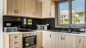 A modern kitchen with wooden cabinets, a built-in oven, a microwave, and a large window offering a view of the outside.