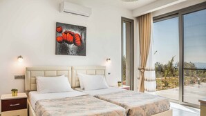 A double bed with a beige headboard, a nightstand with a lamp, and a painting of red flowers on the wall.
