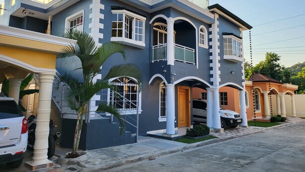 A modern two-story house with a balcony, large windows, and a driveway.
